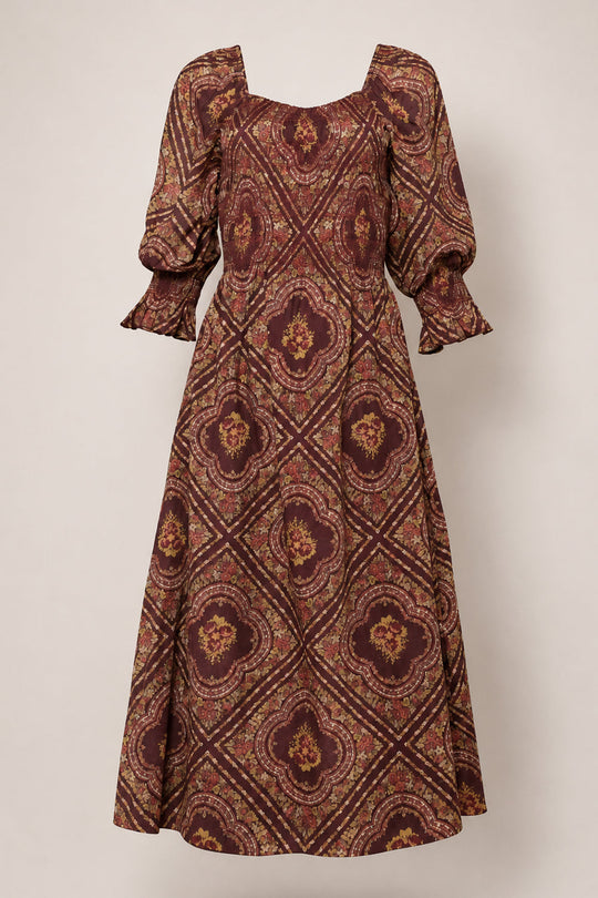 The Josephine Dress in Nocturne Diamond Rose by Ivy City Co features a burgundy and gold patterned cotton design with a smocked bodice, puffed three-quarter sleeves, square neckline, and a flared, ankle-length skirt. Maternity friendly for added comfort and style, it’s displayed on a plain background.