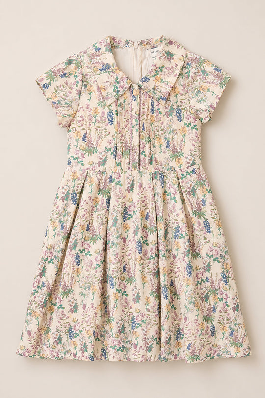 The Mini Amber Dress in Autumn Bouquet by Ivy City Co is a short-sleeved girls’ dress featuring a pastel floral pattern, pleated front, and Peter Pan collar. This charming viscose dress is displayed flat against a neutral background.