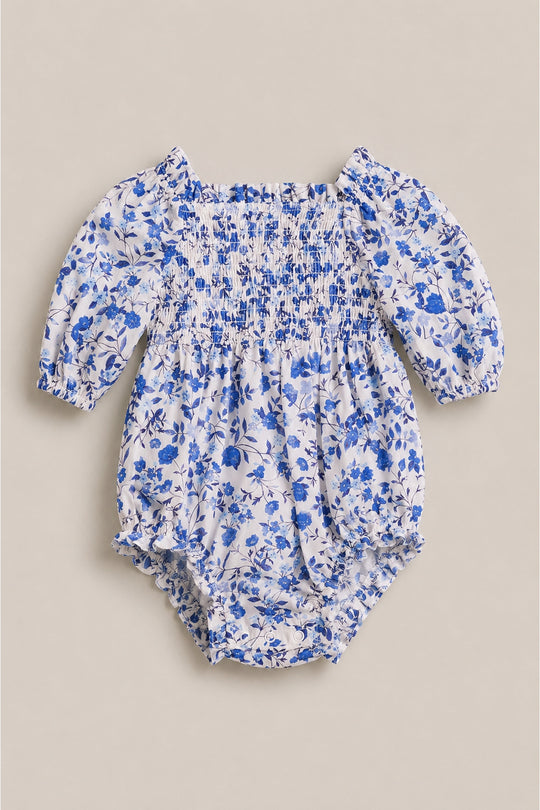 The Ivy City Co Baby Madeline Romper in Ditsy Cobalt Floral features long sleeves, a smocked bodice, and elastic at the cuffs and legs—perfect for cute baby romper outfits or mom and me matching moments.