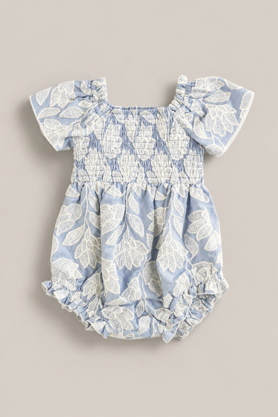 The Ivy City Co Baby Ophelia Romper in Mosaic Embroidery features light blue fabric, short sleeves, white leaf embroidery, smocked chest and waist, and ruffled leg openings for a soft Mom and Me matching look.