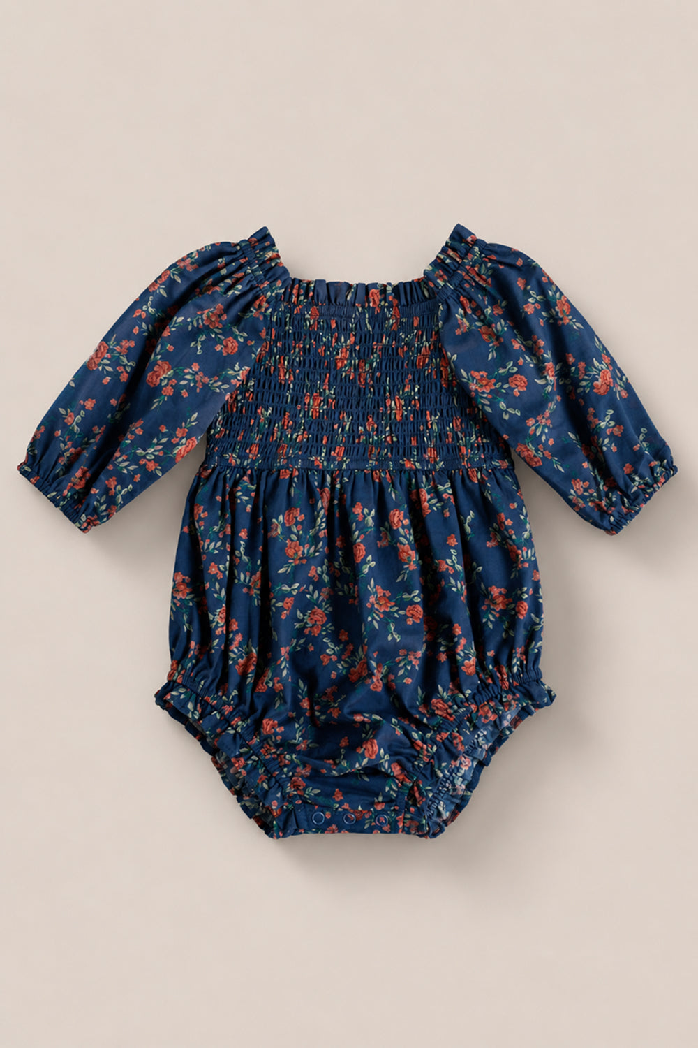 Dress your little one for special occasions in the Baby Madeline Romper in Midnight Vibrant Chintz by Ivy City Co—a navy blue, long-sleeve romper featuring a smocked bodice, small red floral print, and elastic cuffs and leg openings.