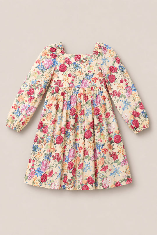 The Mini Adelpha Dress in Autumn Amity Floral by Ivy City Co is a long-sleeve dress featuring a square neckline, elegant balloon sleeves, and a flattering smocked bodice. Its vibrant floral print in shades of red, pink, blue, and green decorates a light yellow background. The dress is displayed laid flat on a neutral surface.