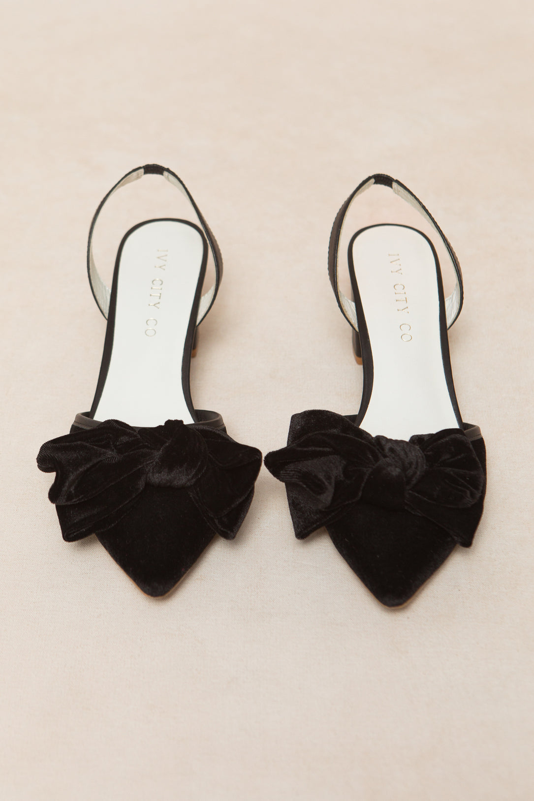 The Eloise Bow Heel in Black by Ivy City Co features elegant black pointed toes and large velvet bows, reminiscent of classic black bow heel styles, and is displayed on a neutral light background.