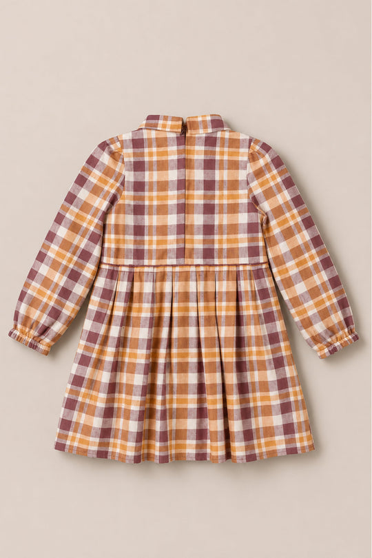The Mini Bowie Long Sleeve Dress in Spiced Plaid by Ivy City Co is a children’s long-sleeve cotton dress featuring a fitted bodice, gathered skirt, and elasticized cuffs. Showcased from the back on a neutral background, it displays a plaid pattern in shades of brown, yellow, and white.