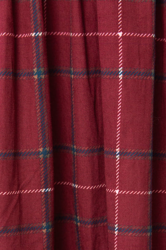 A close-up of the Hattie Dress in Burgundy Plaid by Ivy City Co highlights its white, blue, and black plaid fabric and gathered seam detail—perfect for a stylish midi-length look.