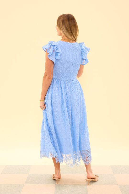 Woman wearing a blue dress with ruffled sleeves and lace hem on a beige background