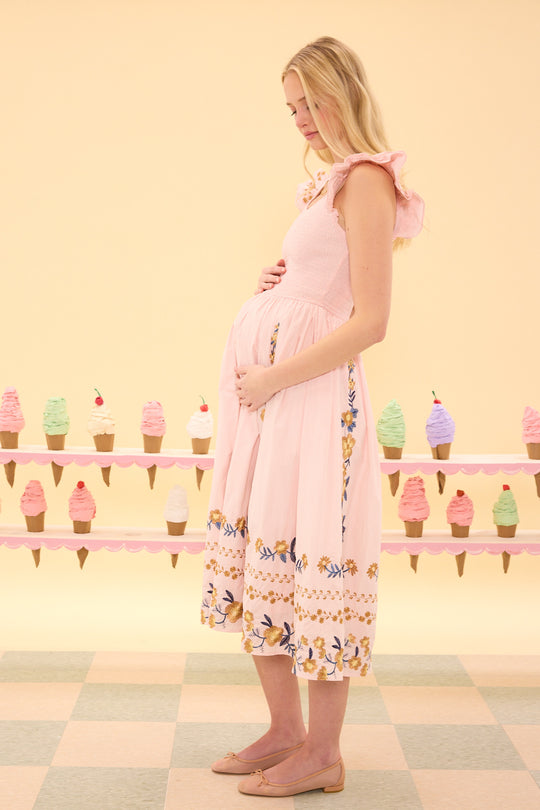 Pregnant woman in a pink dress standing in front of an ice cream stand with colorful ice cream cones.