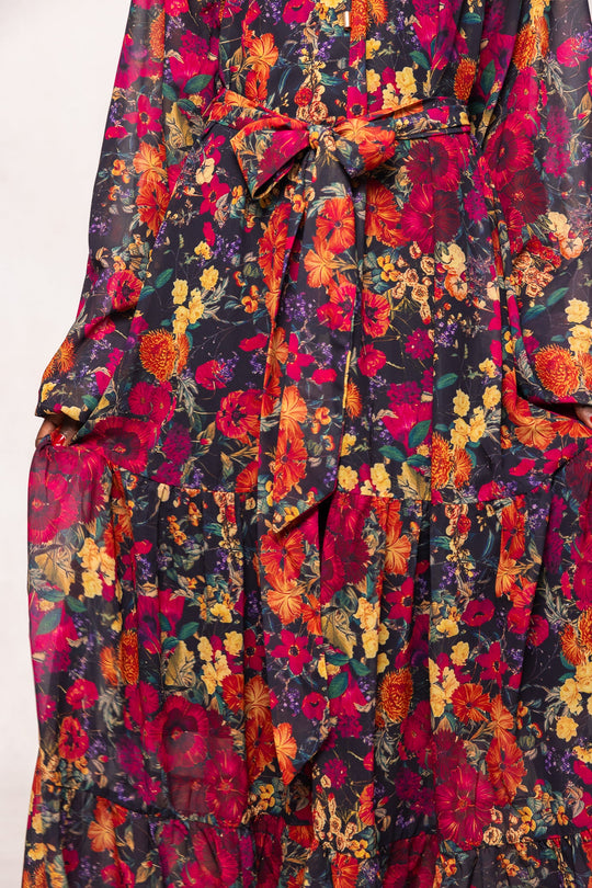 A close-up of the Imogen Dress in Night Garden by Ivy City Co—a long sleeve maxi dress adorned with a vibrant red, yellow, and orange floral pattern, complete with a matching fabric belt tied at the waist—making it a perfect maternity-friendly fall floral maxi dress.