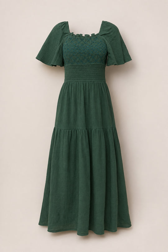 The Jade Dress in Evergreen by Ivy City Co is a dark green, ankle-length cotton dress featuring short flutter sleeves, a smocked square neckline, a fitted waist, and a tiered skirt. Maternity friendly and shown against a plain light beige background.