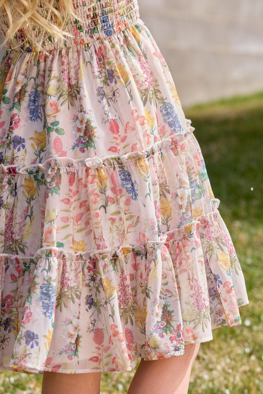 Close-up of the Ivy City Co Mini Madeline Dress in Cordelia Floral, featuring a light ruffled skirt with pink, purple, and yellow flowers—perfect for a girl's birthday outdoors on sunny days.