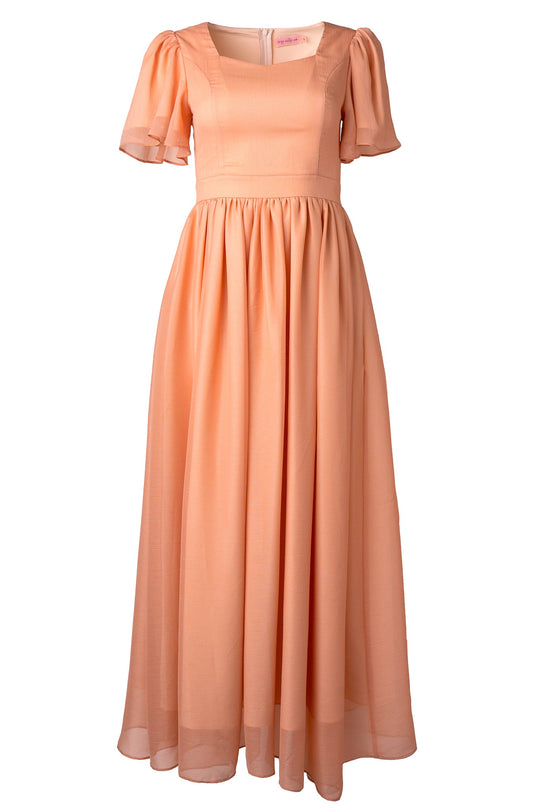 The Abbie Dress in Apricot Crush by Ivy City Co showcases a peach-toned, floor-length silhouette with short puff sleeves and a fitted bodice. Its lightweight, sheer fabric forms a flowing pleated skirt, making this elegant maxi dress an ideal choice for bridesmaids or special occasions.