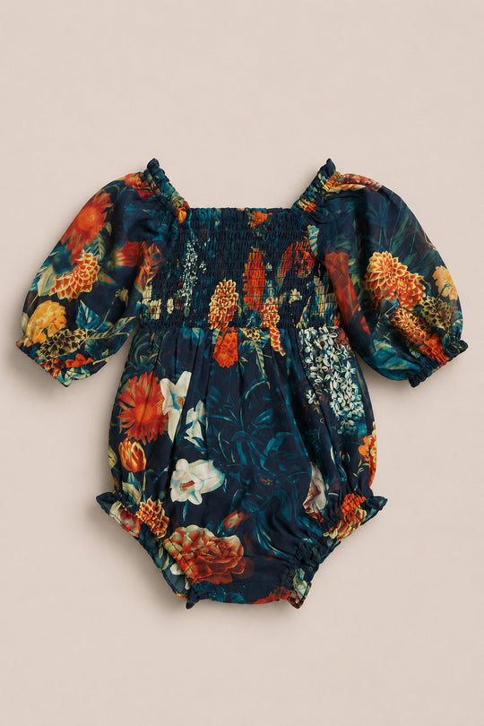 Introducing the Baby Madeline Romper in Imogen Moody Floral by Ivy City Co—a darling chiffon romper adorned with a striking dark floral pattern of red, yellow, and white blooms set against a navy blue backdrop. This charming piece features puffed short sleeves and is beautifully finished with a smocked bodice for enhanced style and comfort.
