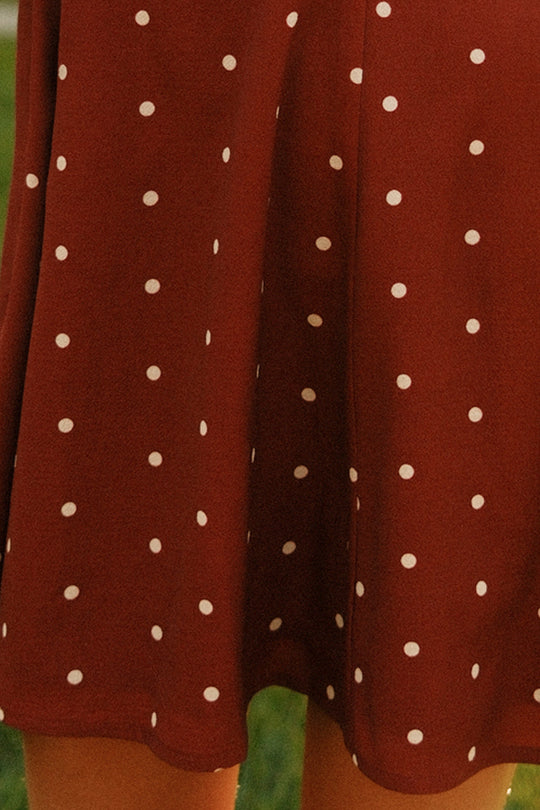 A close-up of the Teen Blakely Dress in Cranberry Dainty Dot by Ivy City Co, featuring delicate white polka dots and petal sleeves, worn outdoors.