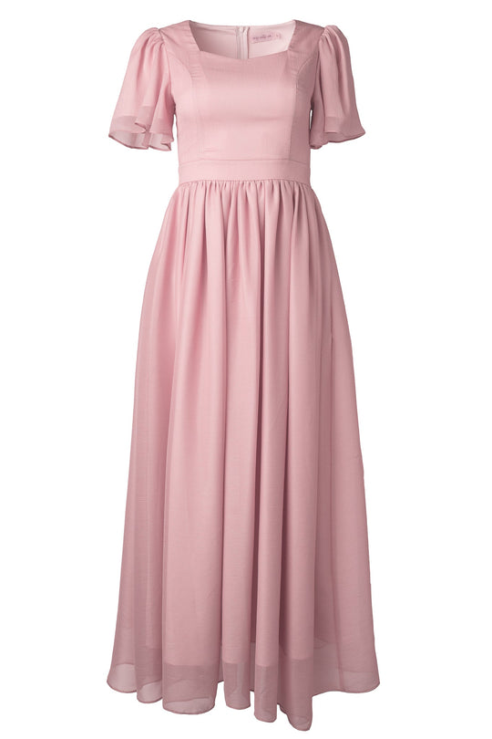 The Abbie Dress in Blush by Ivy City Co is a long maxi dress featuring short flutter sleeves and a fitted bodice, crafted from a flowy, semi-sheer fabric. Displayed against a white background, it’s an elegant and modest option for bridesmaids.