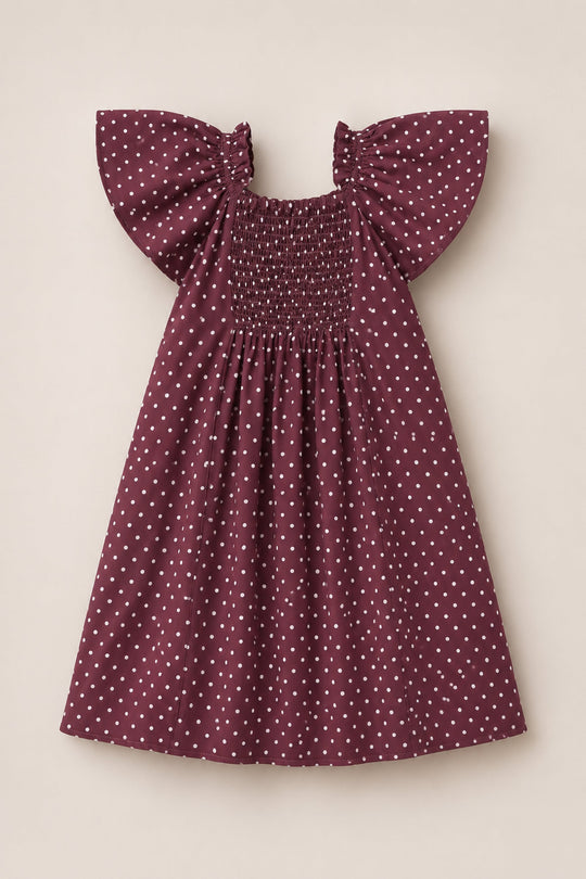 An Ivy City Co Teen Blakely Dress in Aubergine Ditsy Dot, featuring short ruffled sleeves and a smocked bodice, is laid flat on a beige background.