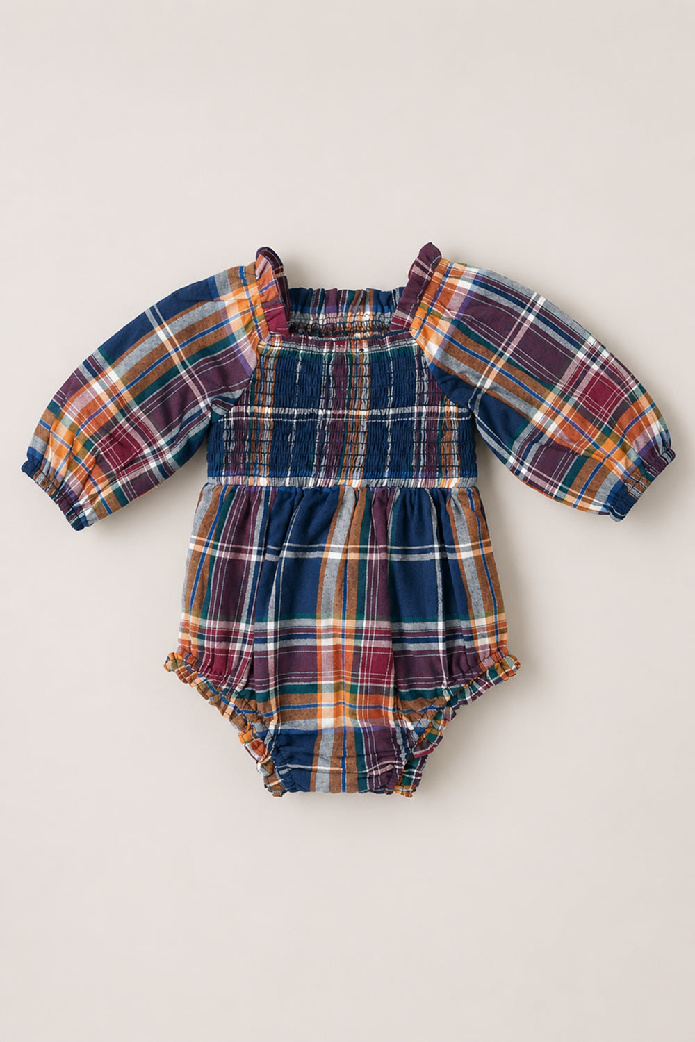 The Ivy City Co Baby Madeline Romper in Midnight Plaid features a charming plaid print in shades of blue, orange, green, and white. Designed with long puff sleeves, an elasticized smocked bodice, and ruffled leg openings, the romper is shown laid flat on a neutral background.